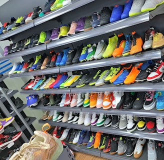 A display of various colorful athletic shoes neatly arranged on multiple shelves. The shoes come in a variety of designs and colors, including neon greens, blues, oranges, and vibrant patterns.